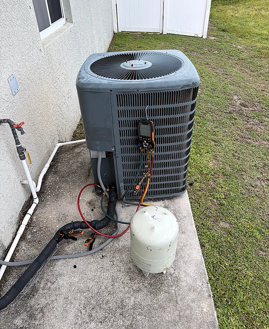 Technician testing refrigerant pressure on an outdoor AC condenser with digital gauges