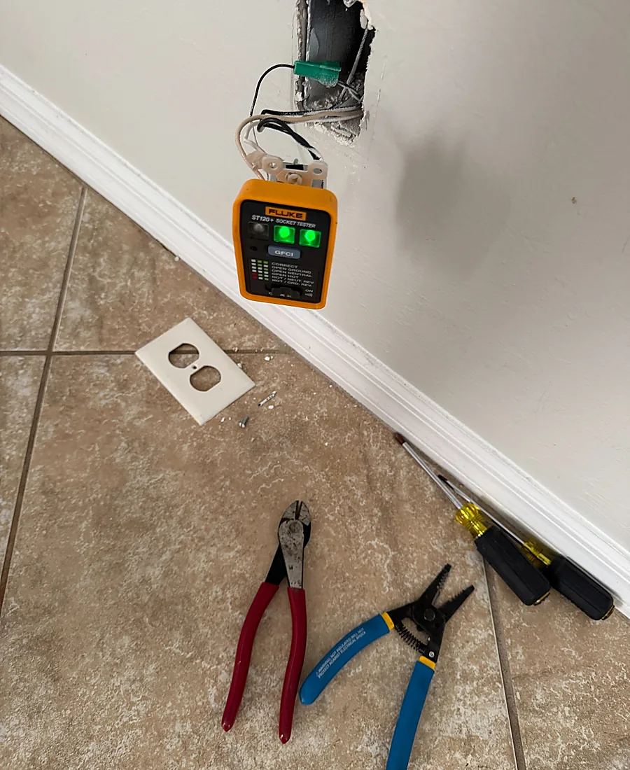 Outlet removed from the wall with a socket tester and tools during repair